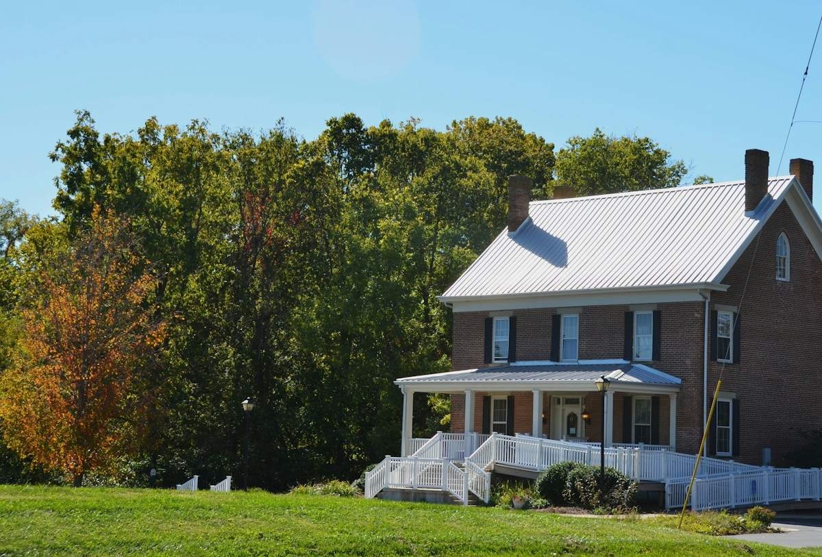 A two-story brick farmhouse with a silver metal roof and a wide porch