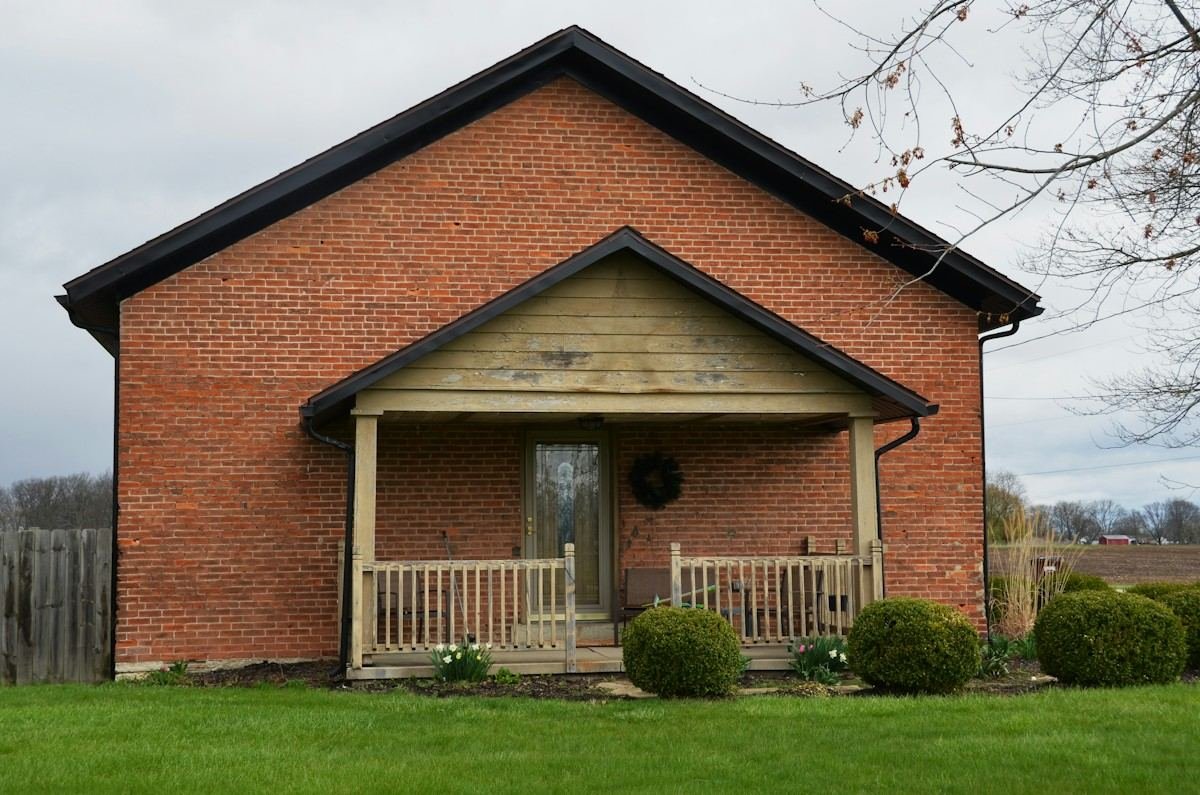 A brick bungalow with a gabled front porch under a cloudy sky