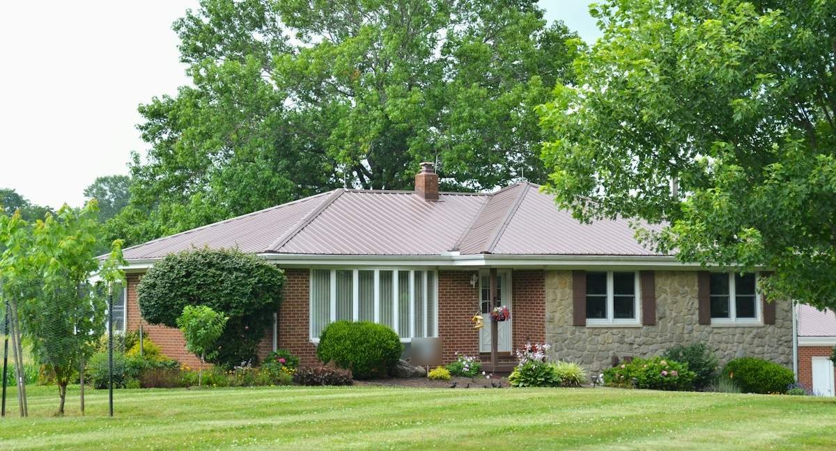 A brick and stone ranch house under tall shade trees