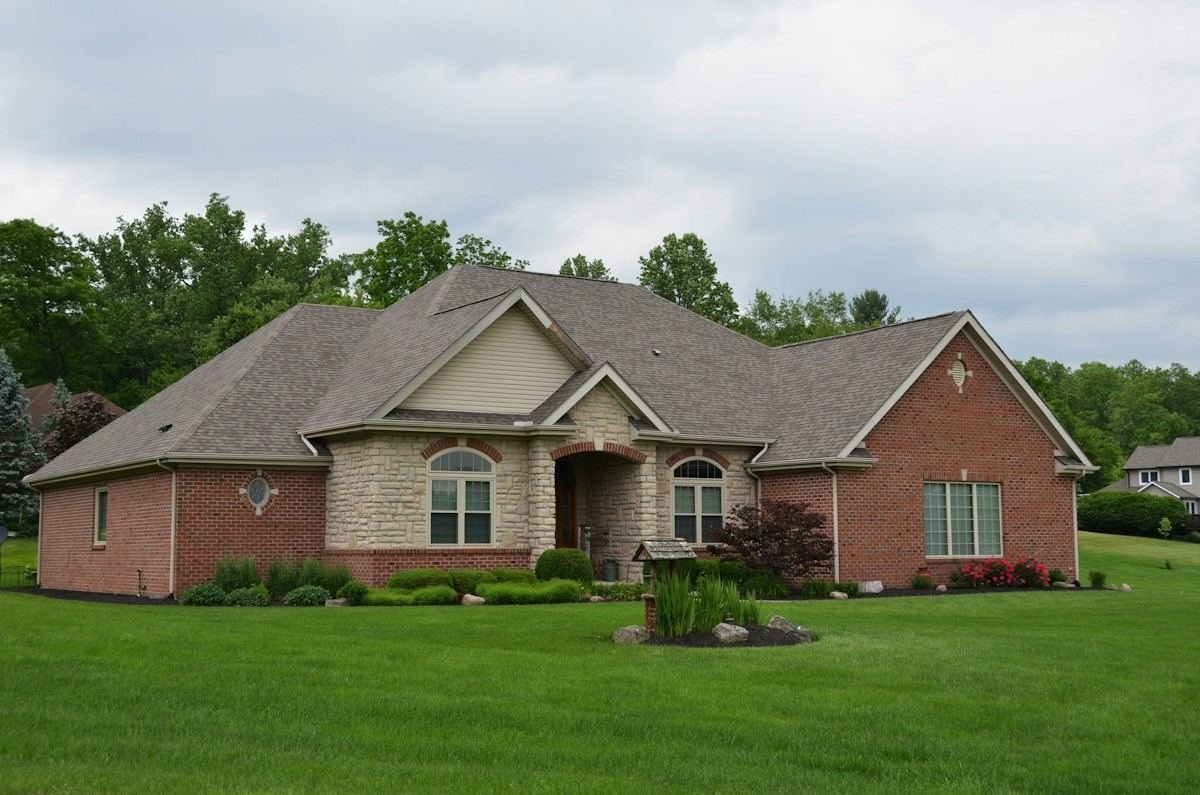 A brick and stone ranch home with a gray shingle roof and a large lawn