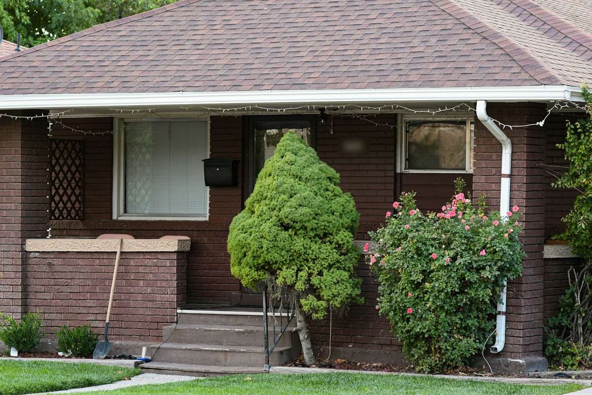 The front porch of a brick bungalow with a brown shingle roof