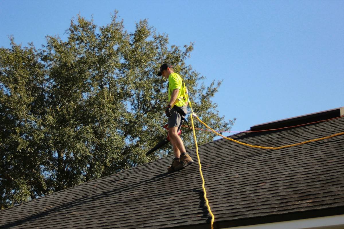 A roofer in a safety harness walking along a shingle roof